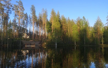 Miilu kuvattuna rannasta päin. - Pohjois-Savossa, Sonkajärven Jyrkän kylällä sijaitsevan Miilu mökin iso terassi, jossa pöytäryhmä 8:lle, kaasugrilli (kesällä) ja  nurmikkoinen takapiha.